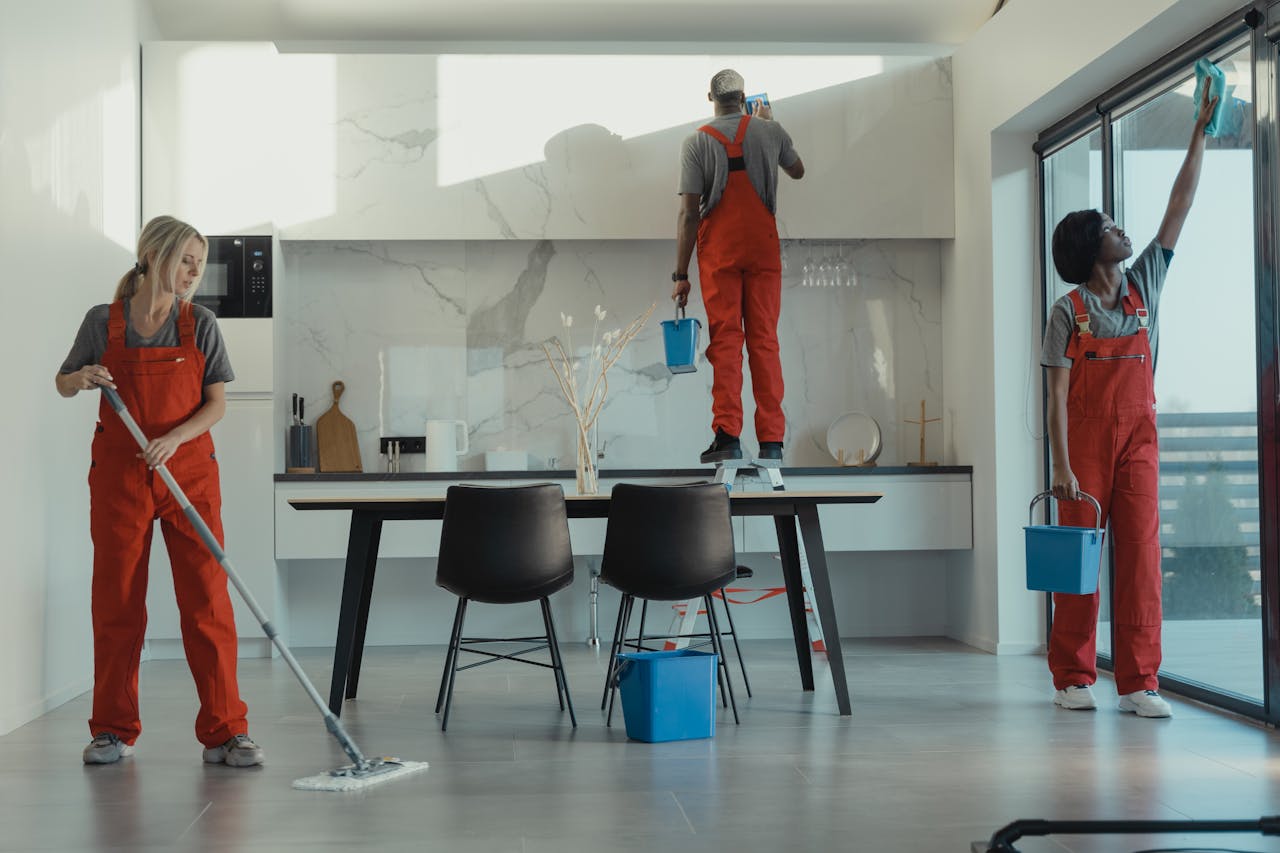 gallery-6 Group of cleaners in red uniforms mopping and wiping glass in a modern dining room.